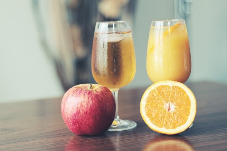 A refreshing display of apple cider and orange juice with fresh apple and orange slices.