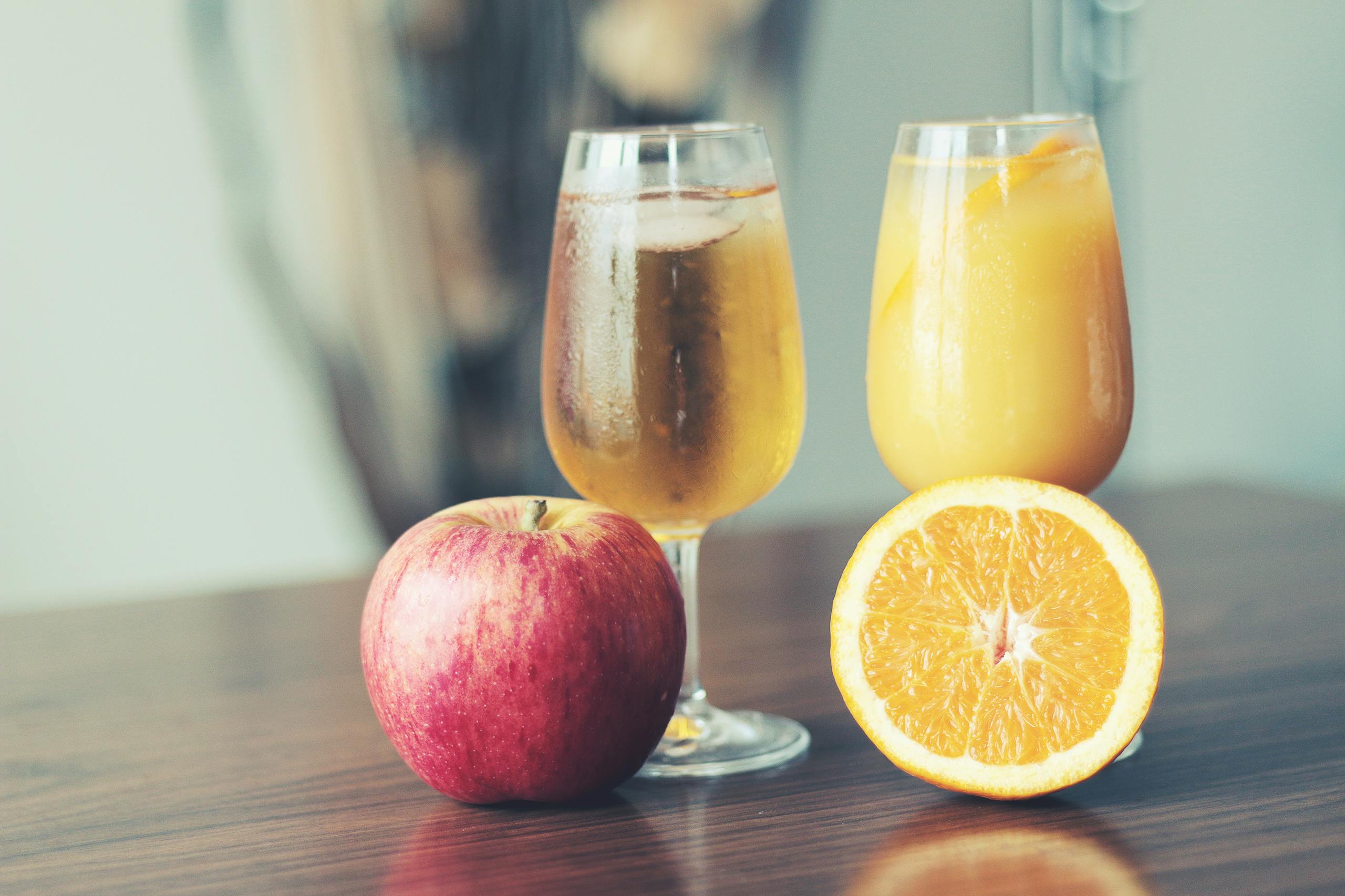 A refreshing display of apple cider and orange juice with fresh apple and orange slices.