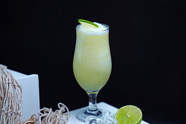 A refreshing lime smoothie in a glass with a lime garnish and ice cubes on the side.