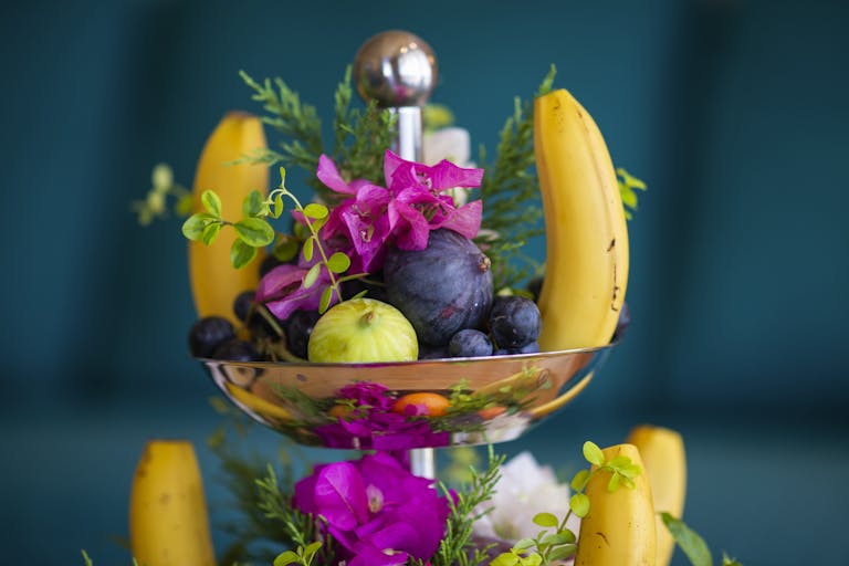 A vibrant arrangement of bananas, figs, and flowers in a decorative bowl.