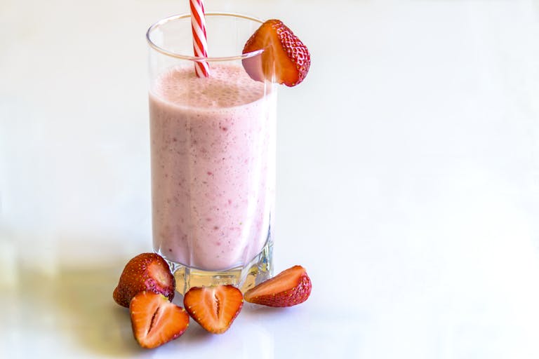 Delicious strawberry smoothie in a glass with fresh strawberries and a striped straw on a light background.