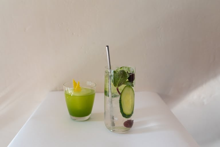 Two refreshing drinks with mint and cucumber garnish on a white table, perfect for a summer setting.