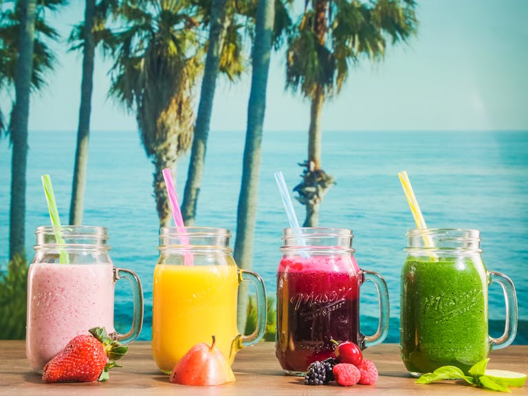 Vibrant smoothies in mason jars with a tropical ocean backdrop, perfect for refreshment.